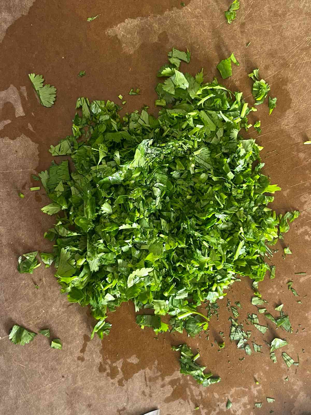 Chopped herbs on a brown cutting board.