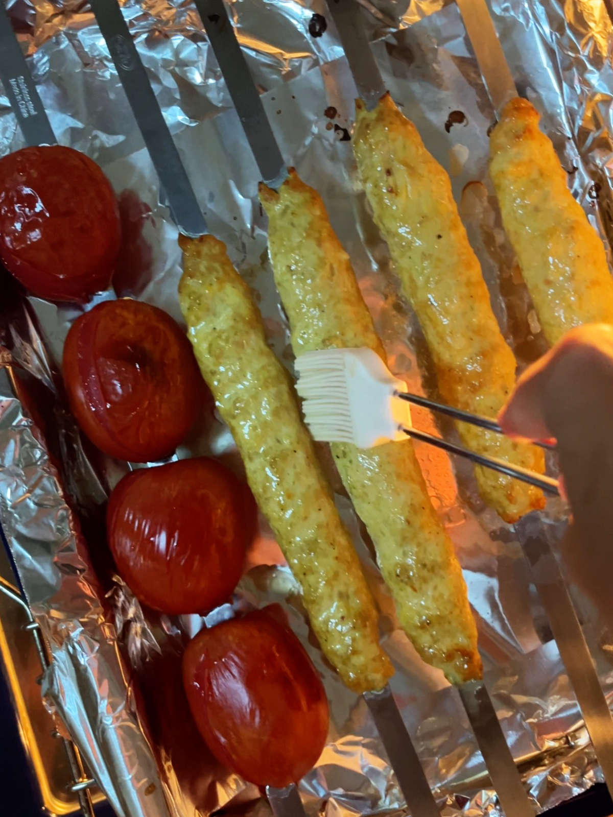 Basting yellow kabobs next to a skewer with four whole tomatoes.