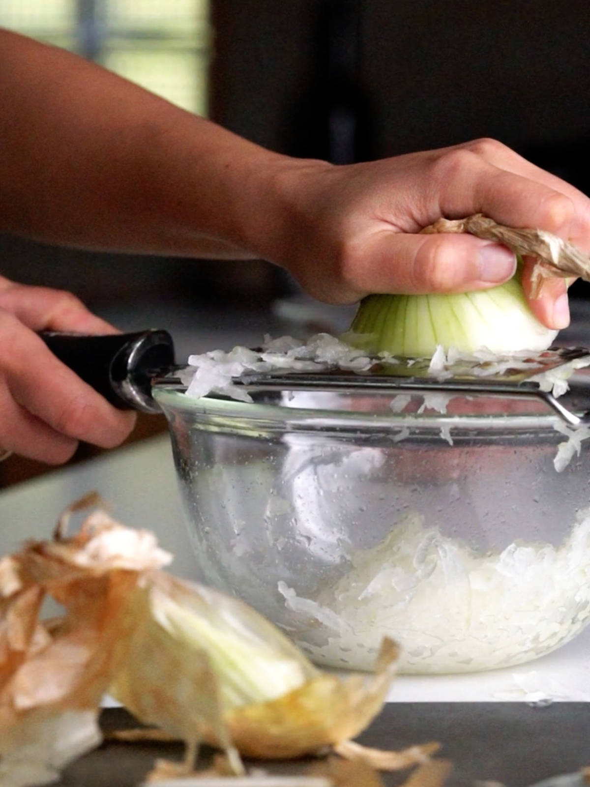 Grating an onion over a glass bowl in front of onion skins.