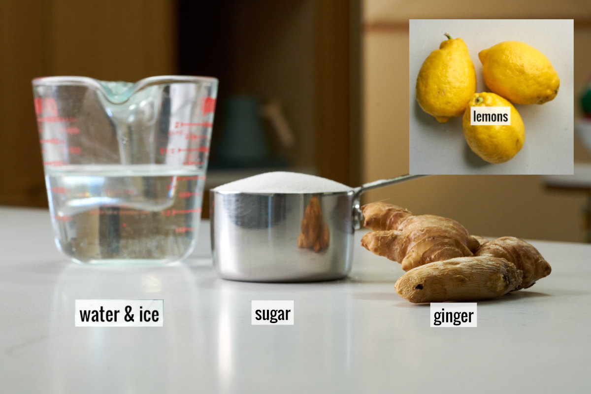 A liquid measuring cup with water next to a measuring cup with sugar and a knob of ginger and three lemons.