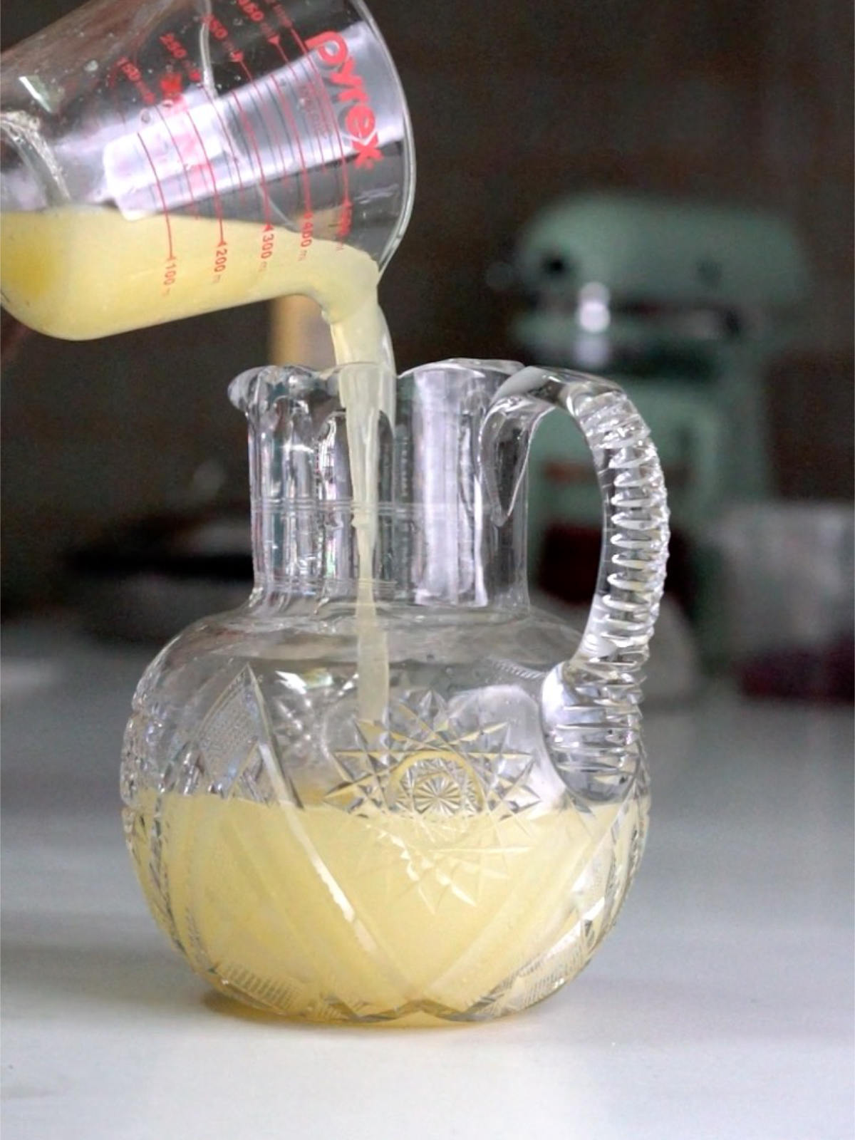 Pouring yellow liquid into a glass pitcher with pale yellow liquid.