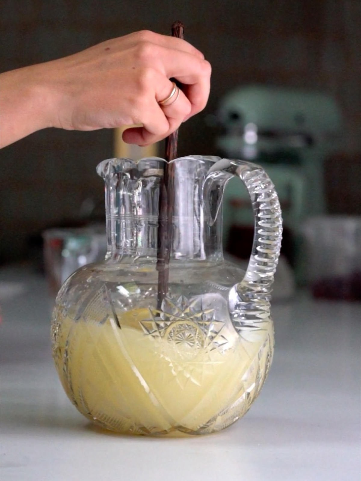 Stirring pale yellow liquid in a glass pitcher with a wood spoon.