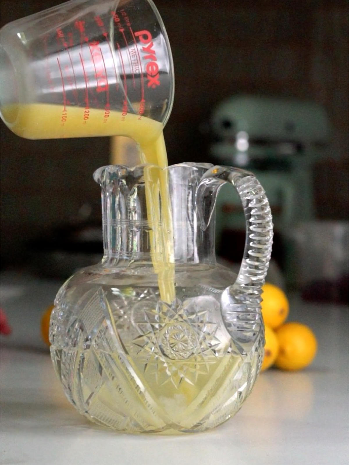 Pouring yellow liquid into a glass pitcher with translucent yellow liquid.