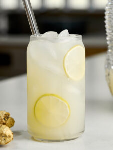 Glass of lemonade with a glass straw next to a knob of ginger.