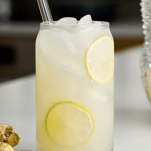 Glass of lemonade with a glass straw next to a knob of ginger.