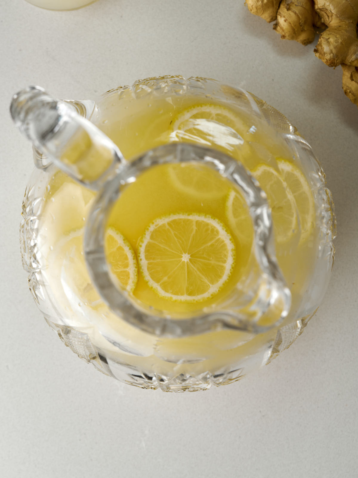 Top view of a pitcher of lemonade with lemon slices next to a knob of ginger.