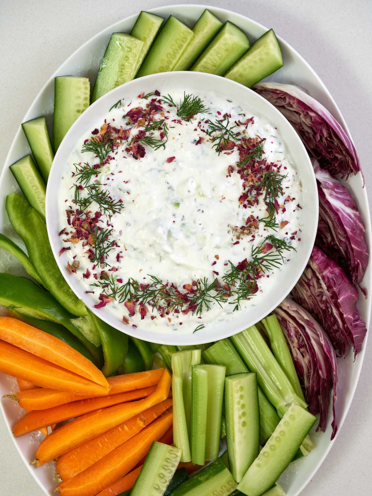 Yogurt dip decorated with dried rose petals and dill on a platter of raw veggies.