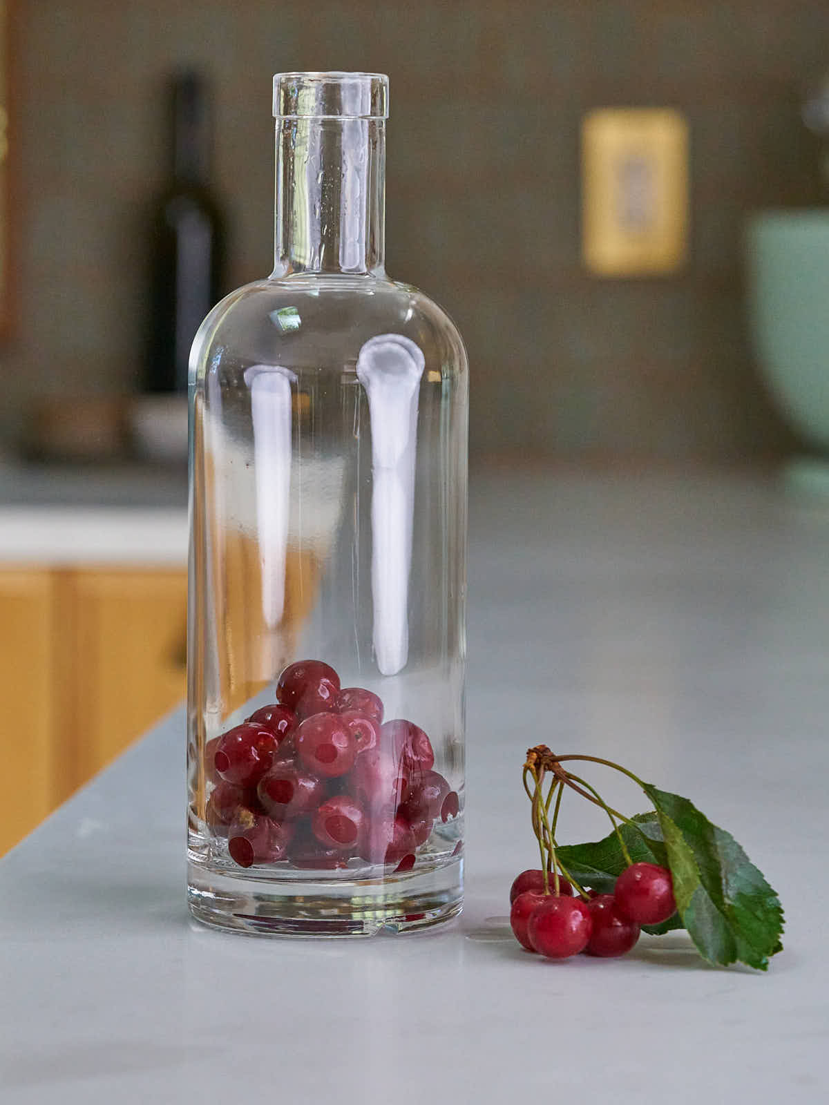 A bottle filled less than half way with cherries next to a bunch of cherries.