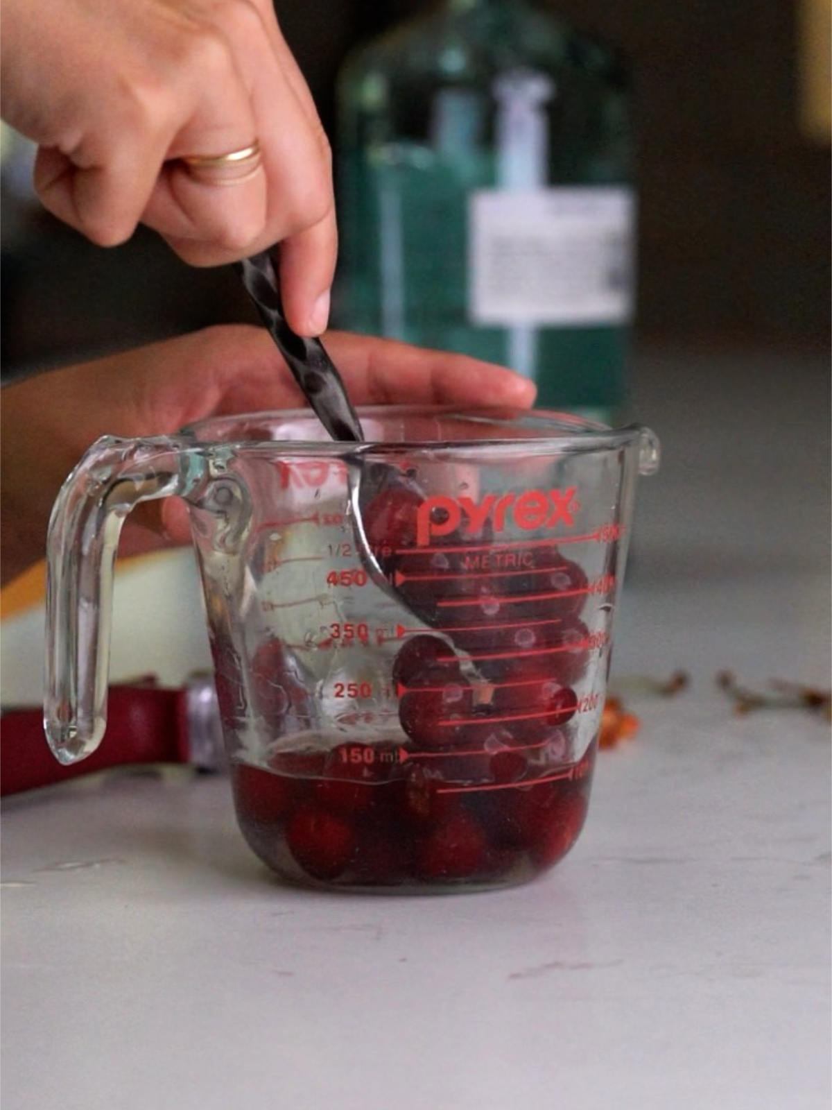 Washing cherries in clear liquid in a glass measuring cup with a metal spoon.