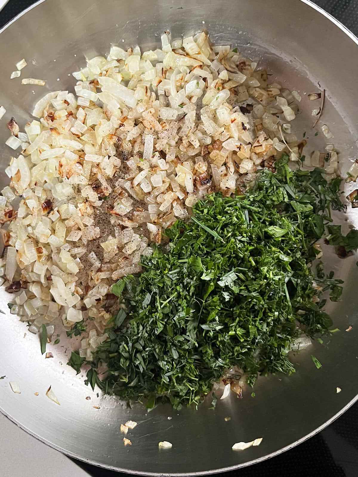 A large silver pot with onions on one side and green herbs on the other.