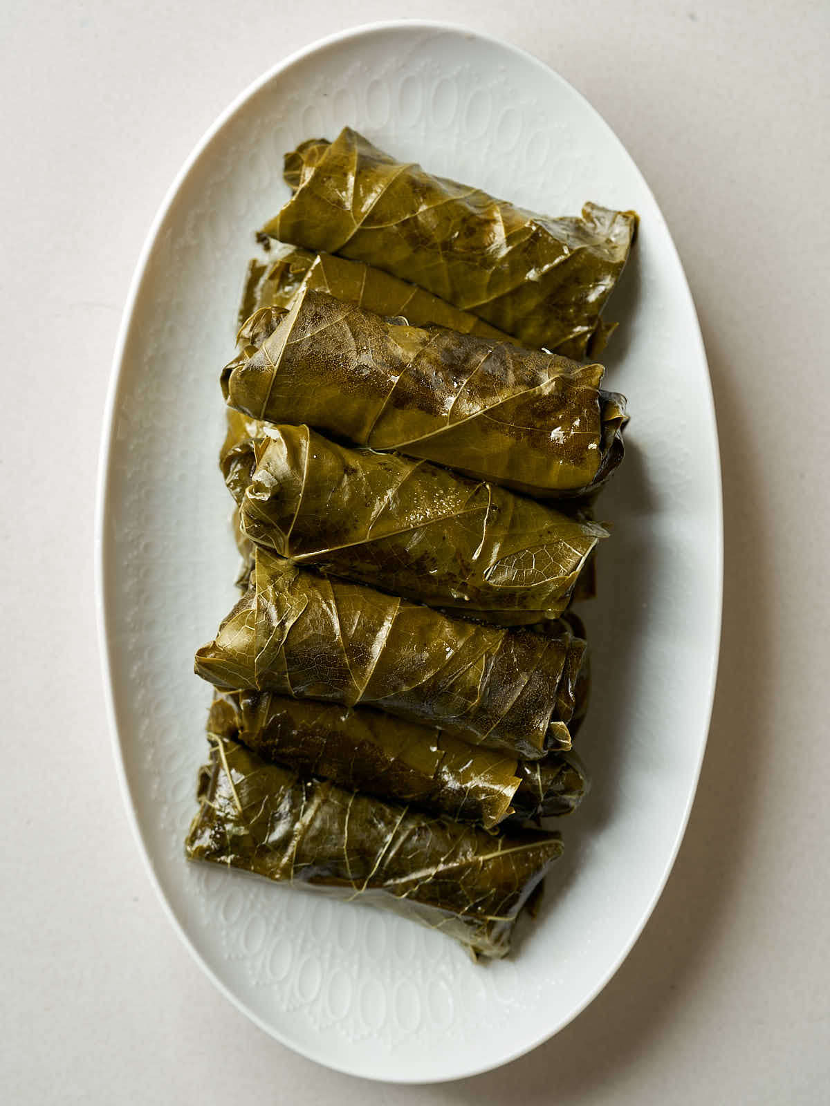 Six rolled grape leaf parcels in a line on a white plate.