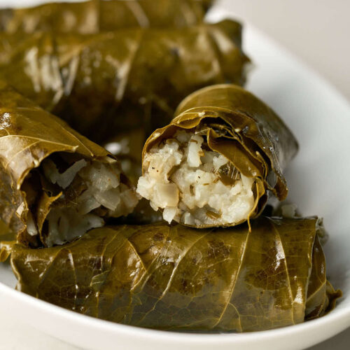 One cut open stuffed grape leaf on a stack of stuffed grape leaves.