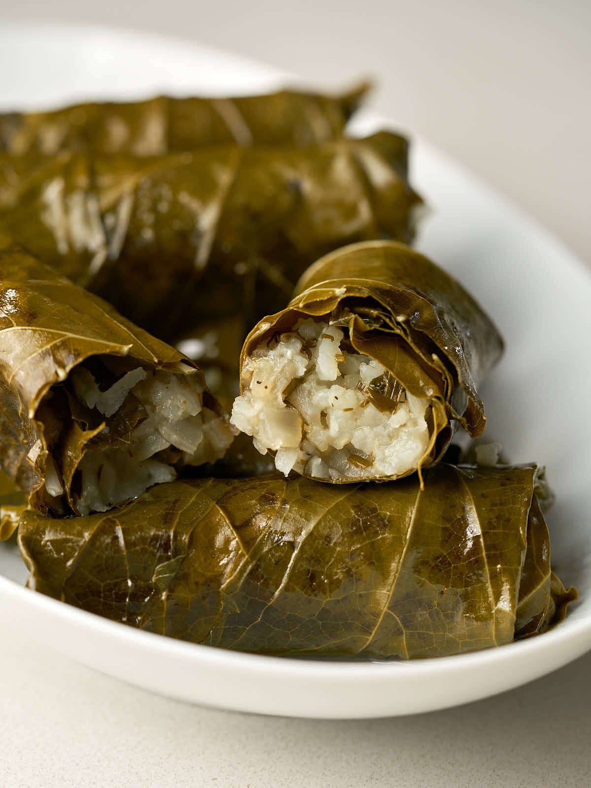 One cut open stuffed grape leaf on a stack of stuffed grape leaves.