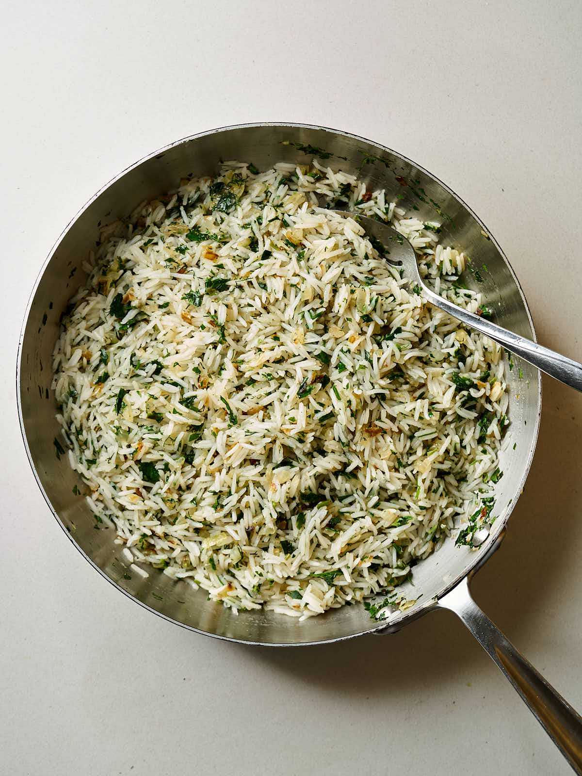 White rice and herbs in a large silver pan with a silver spoon.