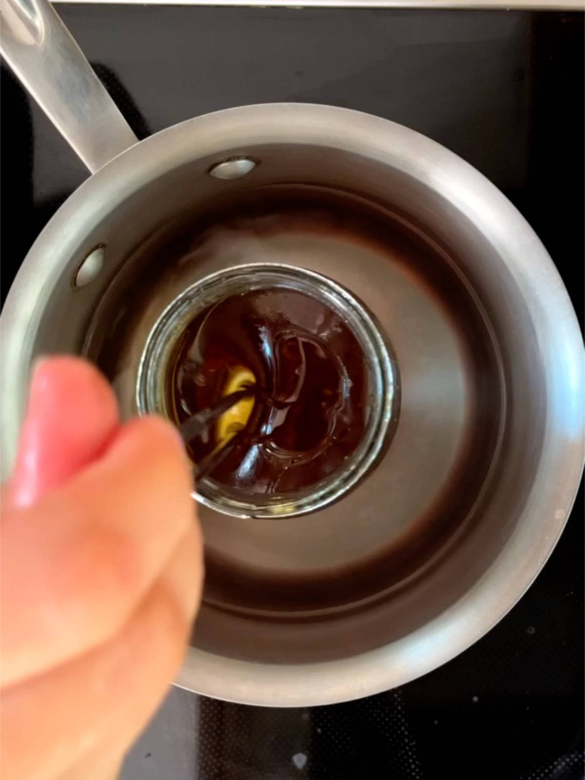 A jar of honey in a metal pot with water in it.