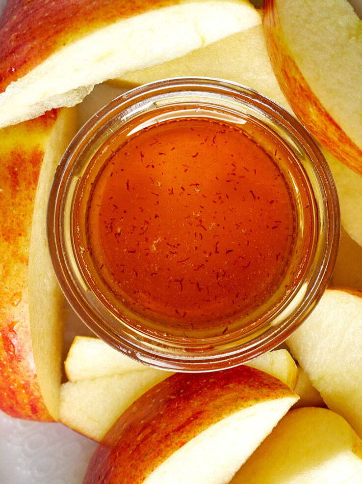 An oval plate of apple wedges with a small dish of honey.