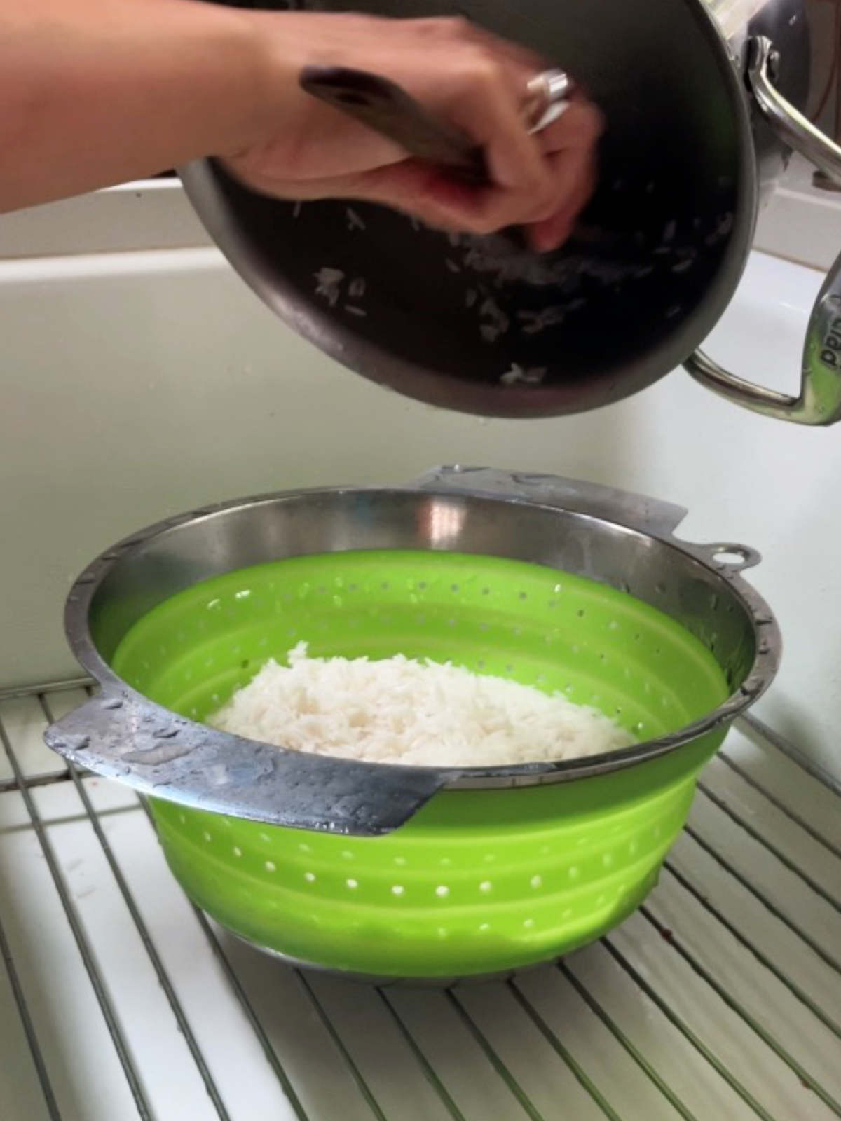 Pouring rice from a metal pot into a green colander in a sink.