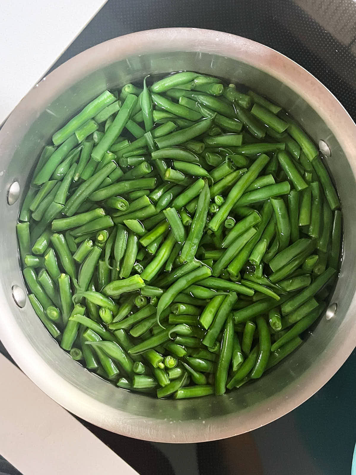 Green beans in a metal pot filled with simmering water.