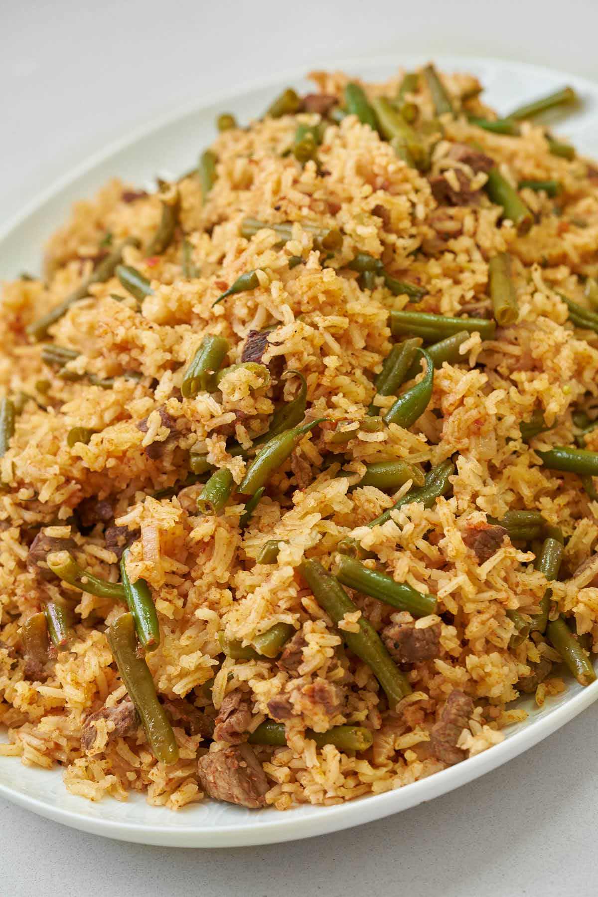 Orange rice studded with green beans on a white platter.