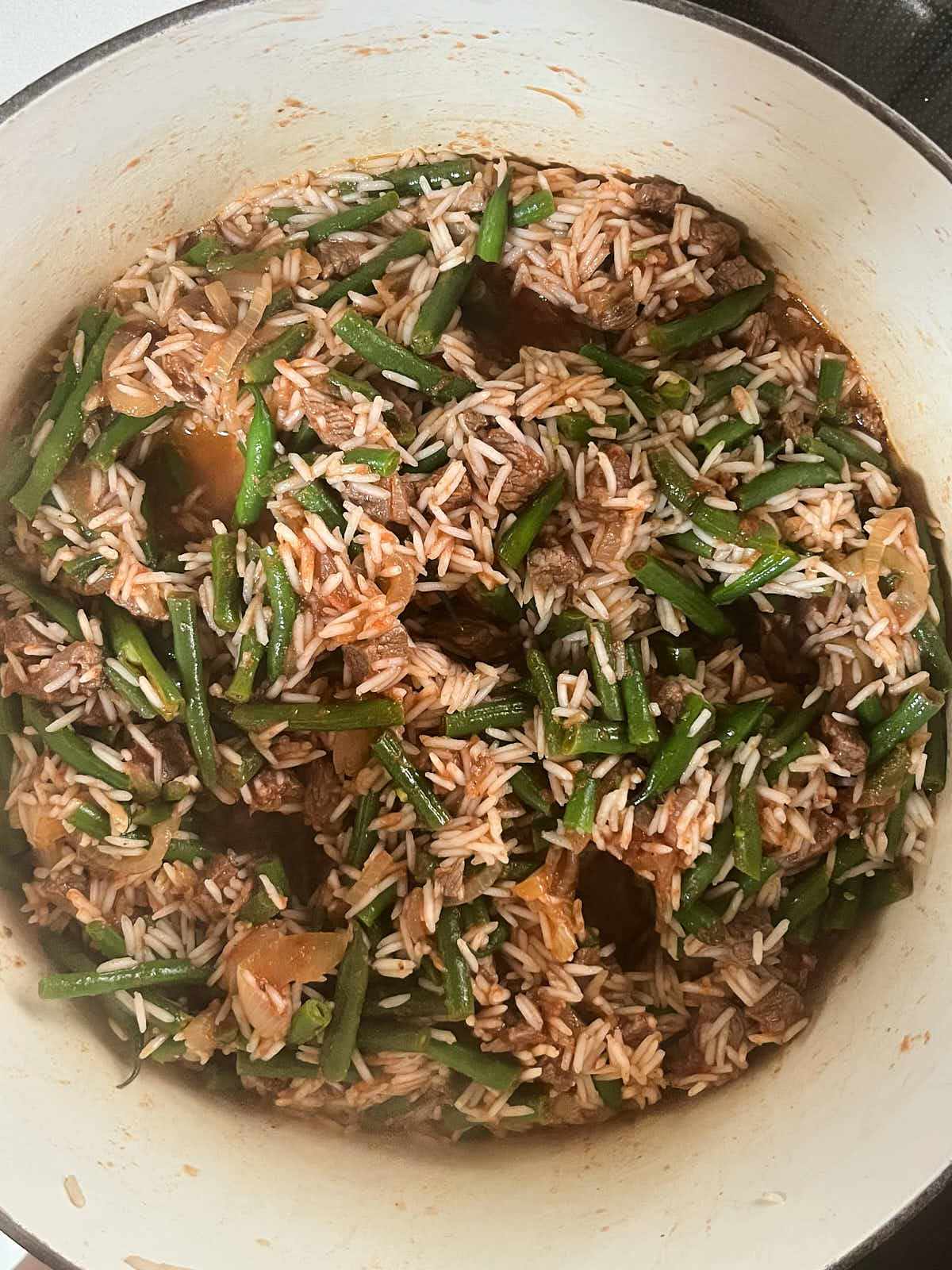 Rice mixed with green beans in an enameled cast iron pot with six holes in the mixture.