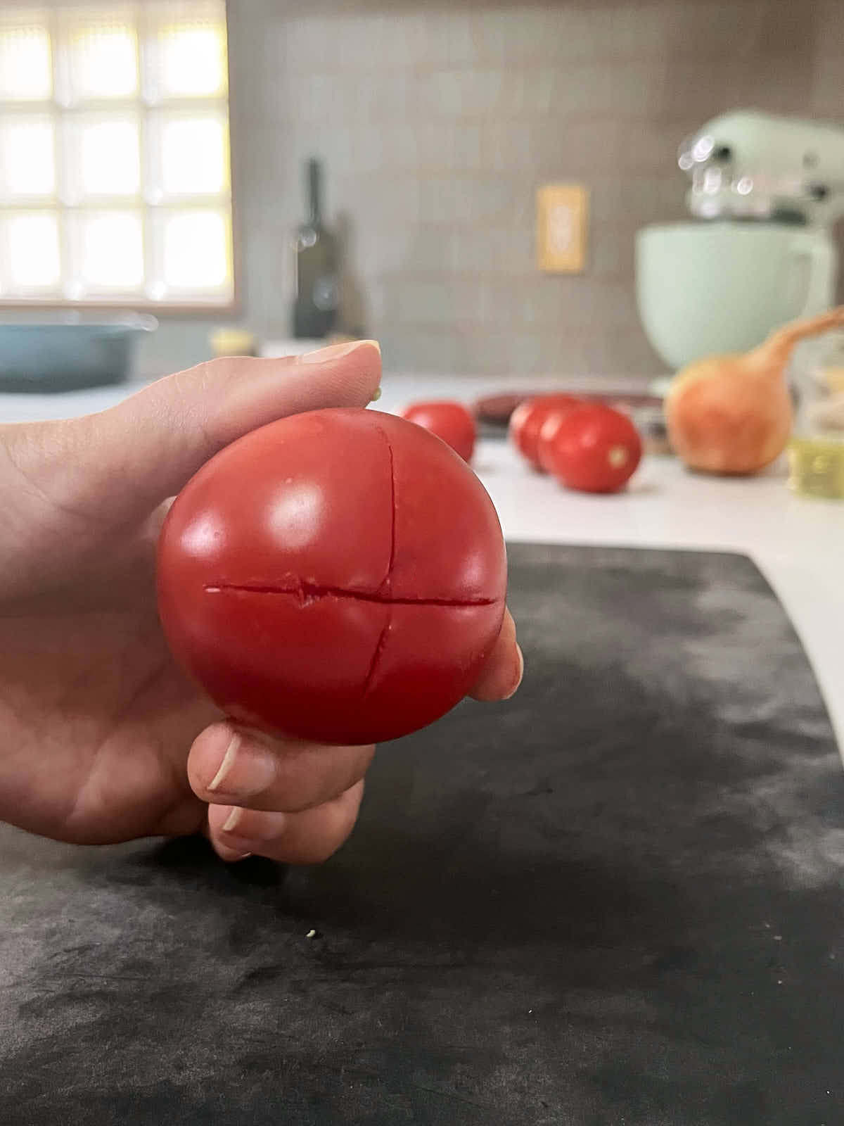 A tomato in a hand with a shallow X on the bottom of it.