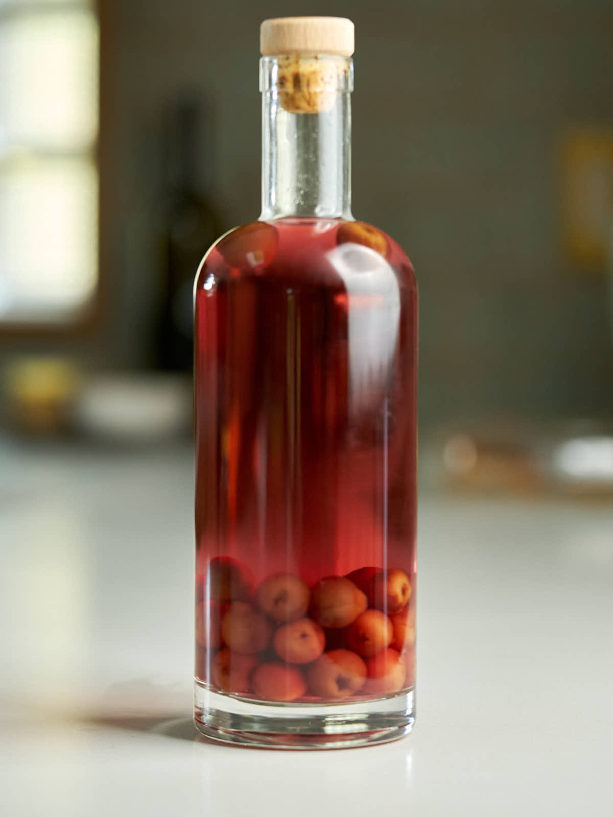 Closed glass bottle filled less than halfway with cherries and the rest of the way with red liquid.