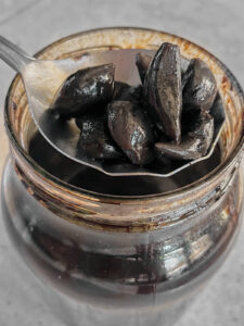 Metal spoon holding black garlic cloves over a jar of black garlic.