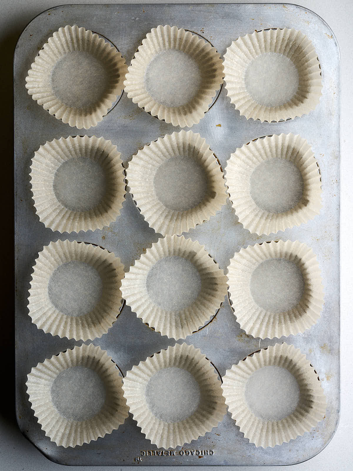 A tin muffin pan with empty muffin paper liners.