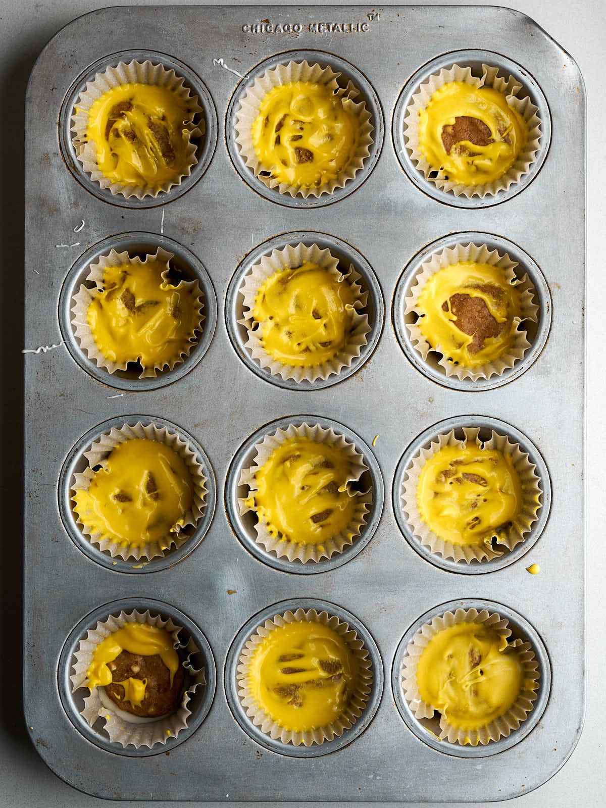 Twelve muffin liners in a pan each filled with yellow chocolate and peanut butter.