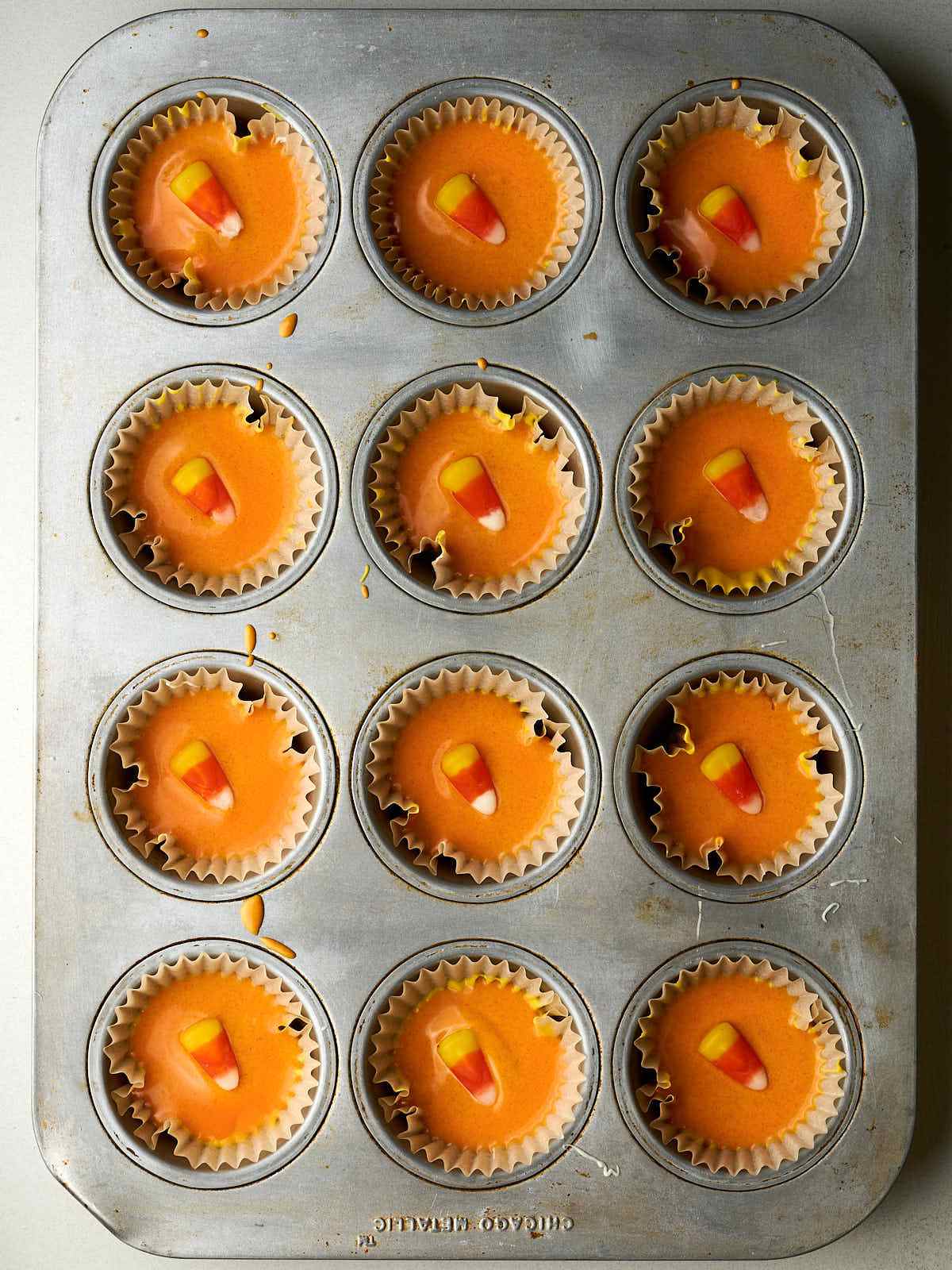 Twelve muffin paper liners with orange chocolate and a candy corn piece on top.