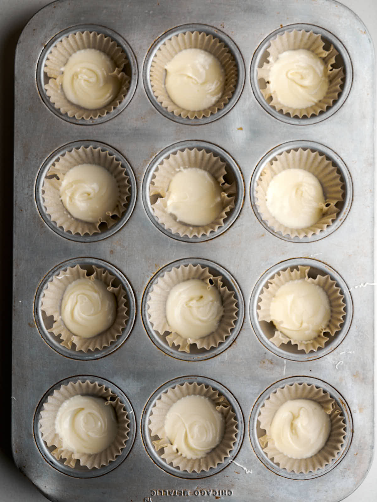 Twelve muffin liners in a pan each filled with a small amount of white chocolate.