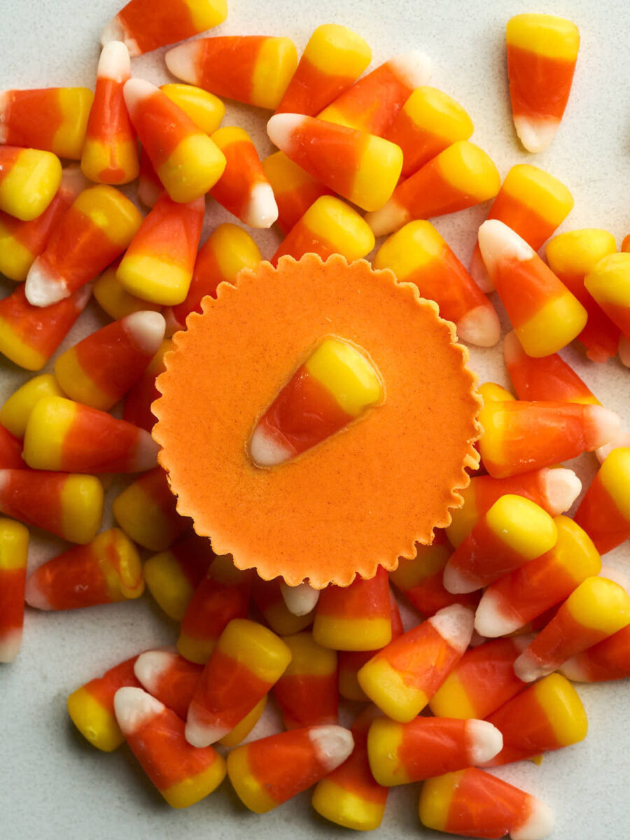 An orange peanut butter cup with a candy corn piece on top of more candy corn.