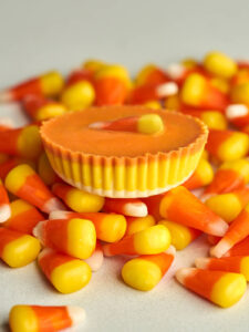 Side view of an orange peanut butter cup with a candy corn piece on top of more candy corn.