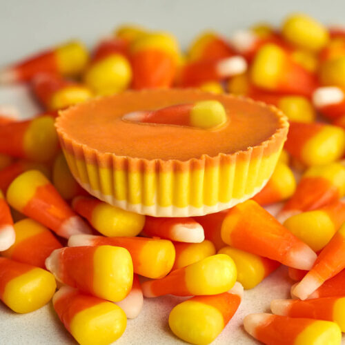 Side view of an orange peanut butter cup with a candy corn piece on top of more candy corn.