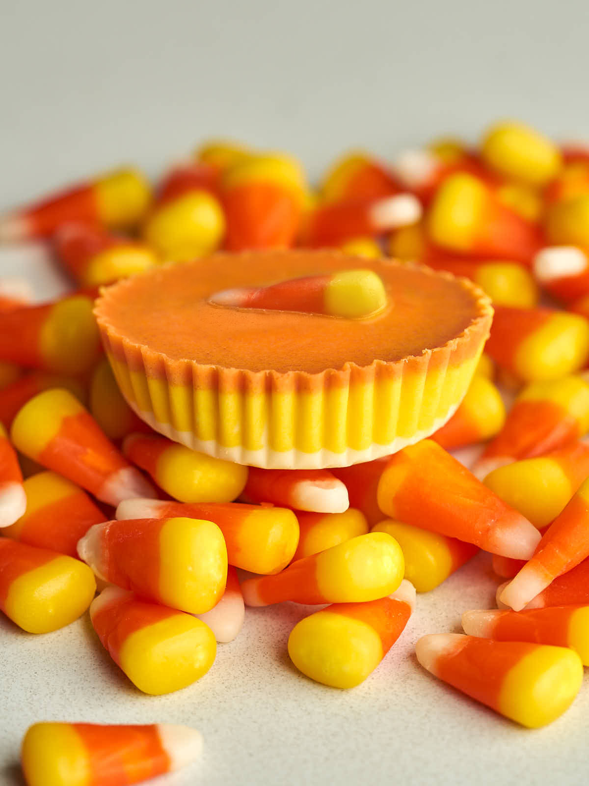 Side view of an orange peanut butter cup with a candy corn piece on top of more candy corn.