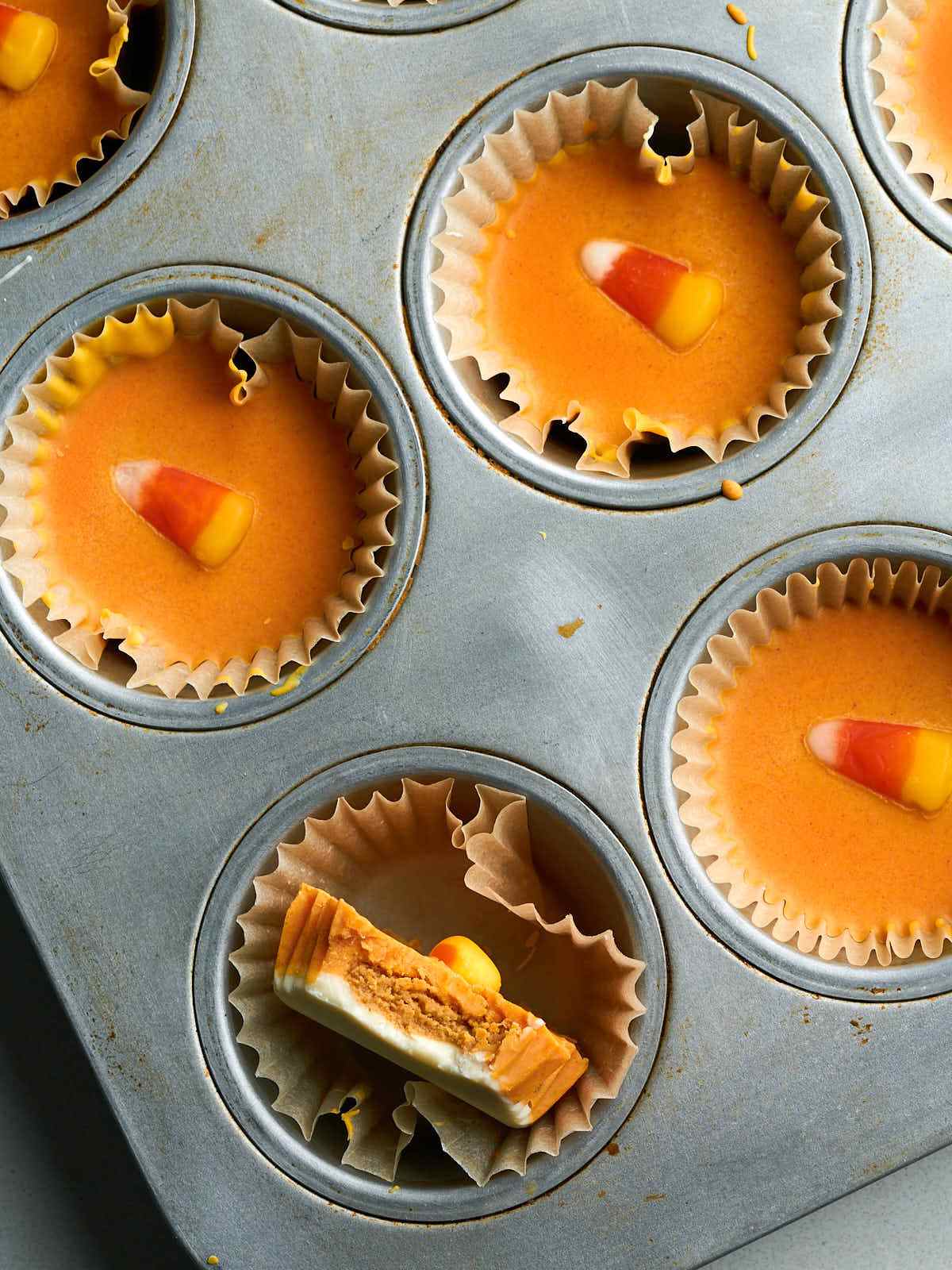 An orange peanut butter cup with a candy corn piece sideways in a muffin tin pan.