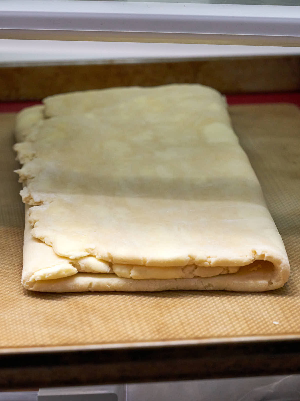 Pastry folded in thirds on a silicone baking mat in the refrigerator.