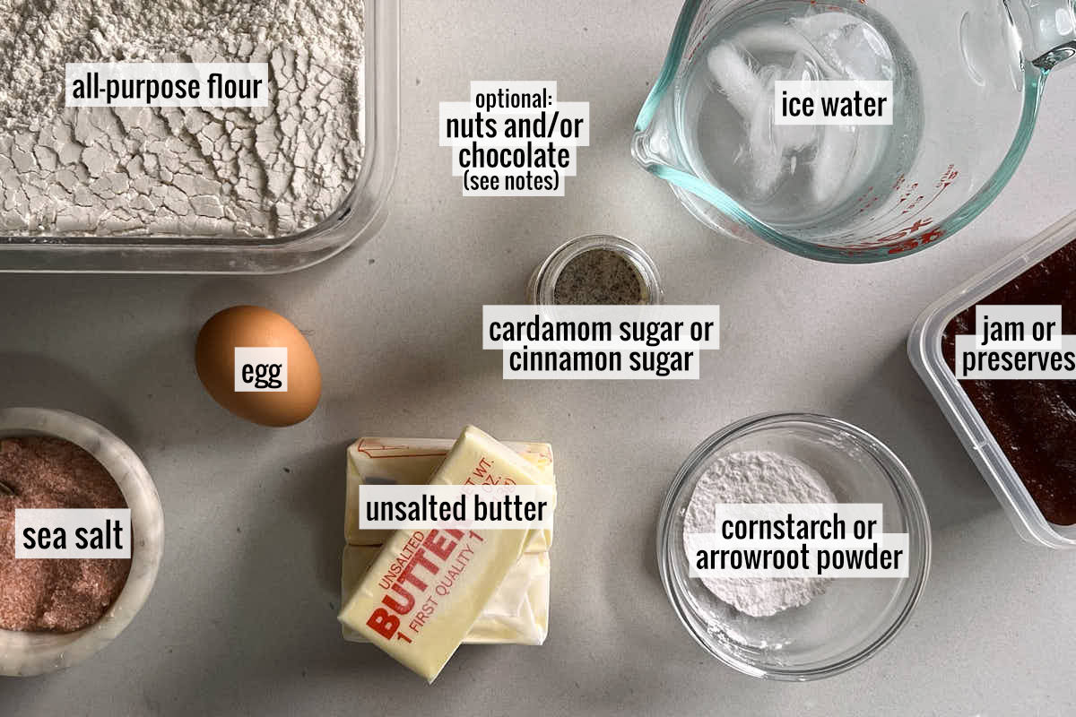 Three sticks of butter next to a square container of flour, an egg, ice water, salt, and other baking ingredients.