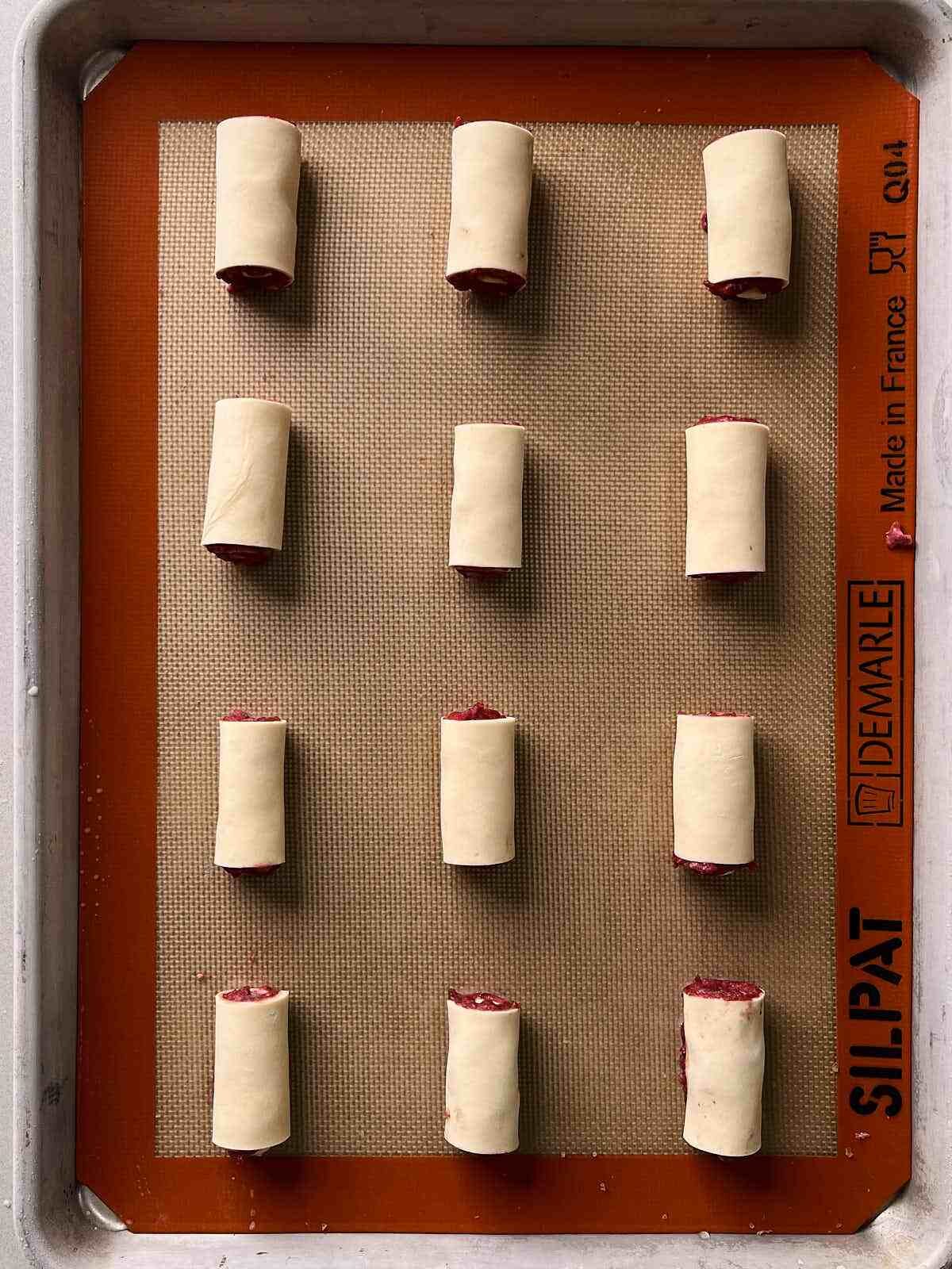 Twelve rolls of pastry dough arranged on a silicone baking mat.