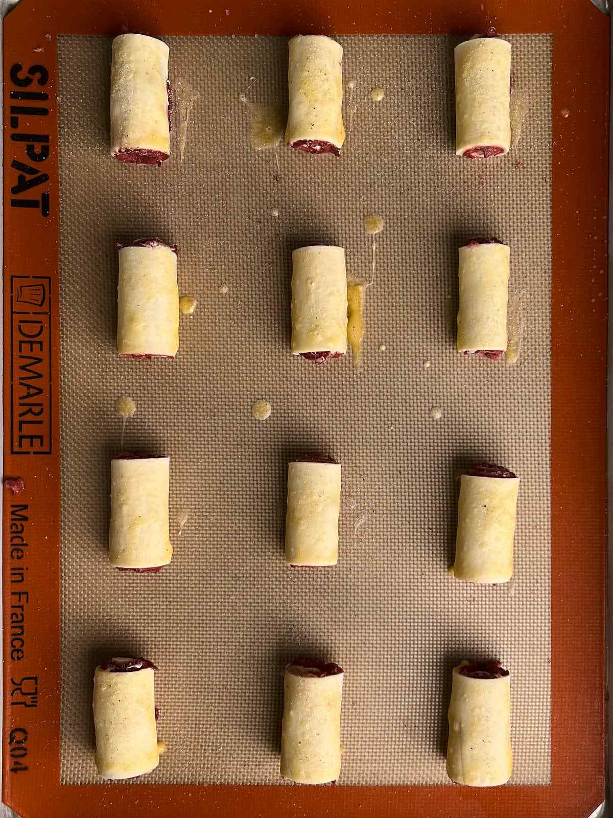 Twelve rolls of pastry dough arranged on a silicone baking mat brushed with gett wash.