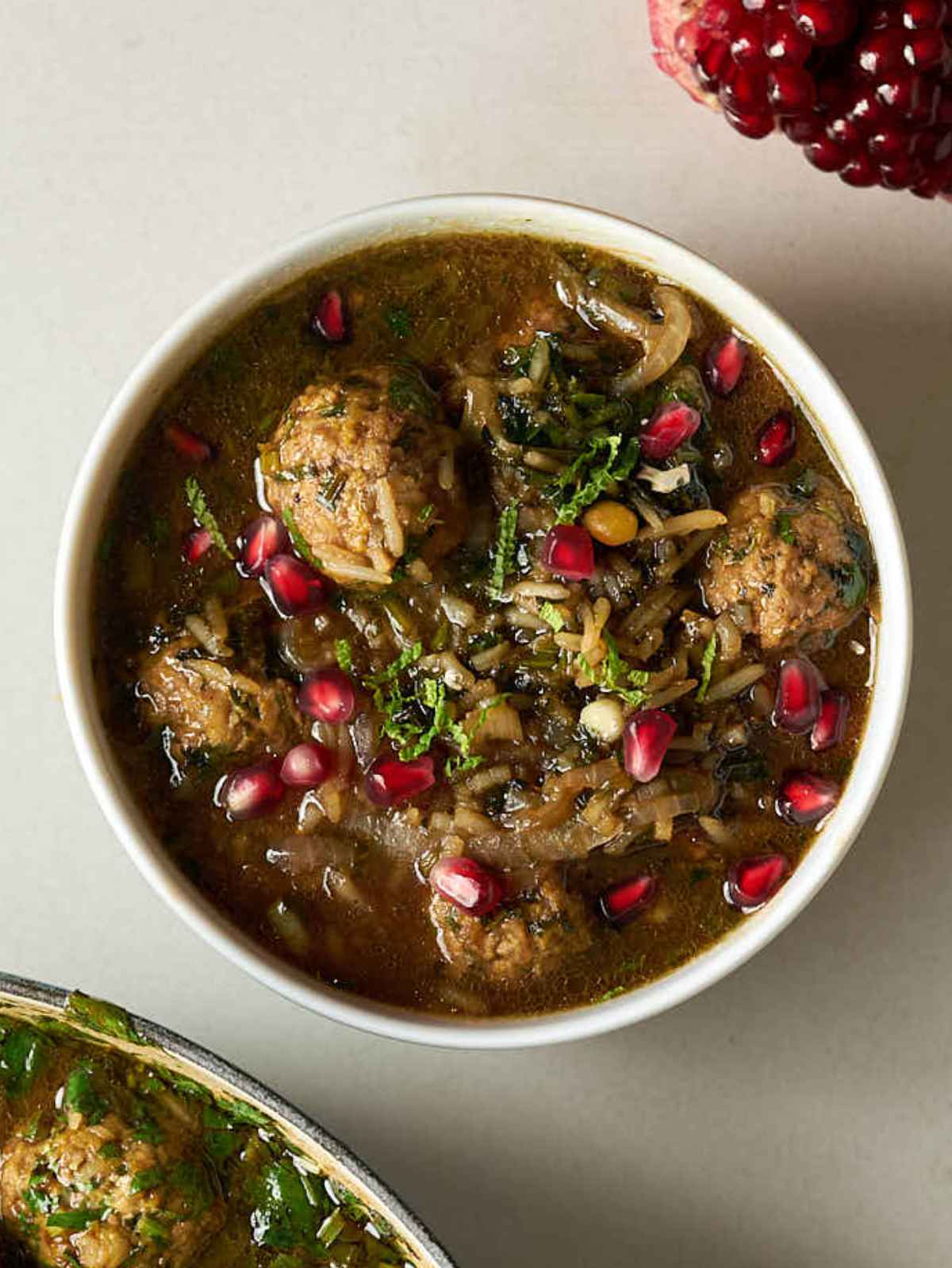 Closeup of a bowl of brown stew with herbs, meatballs, rice, and pomegranate seeds.