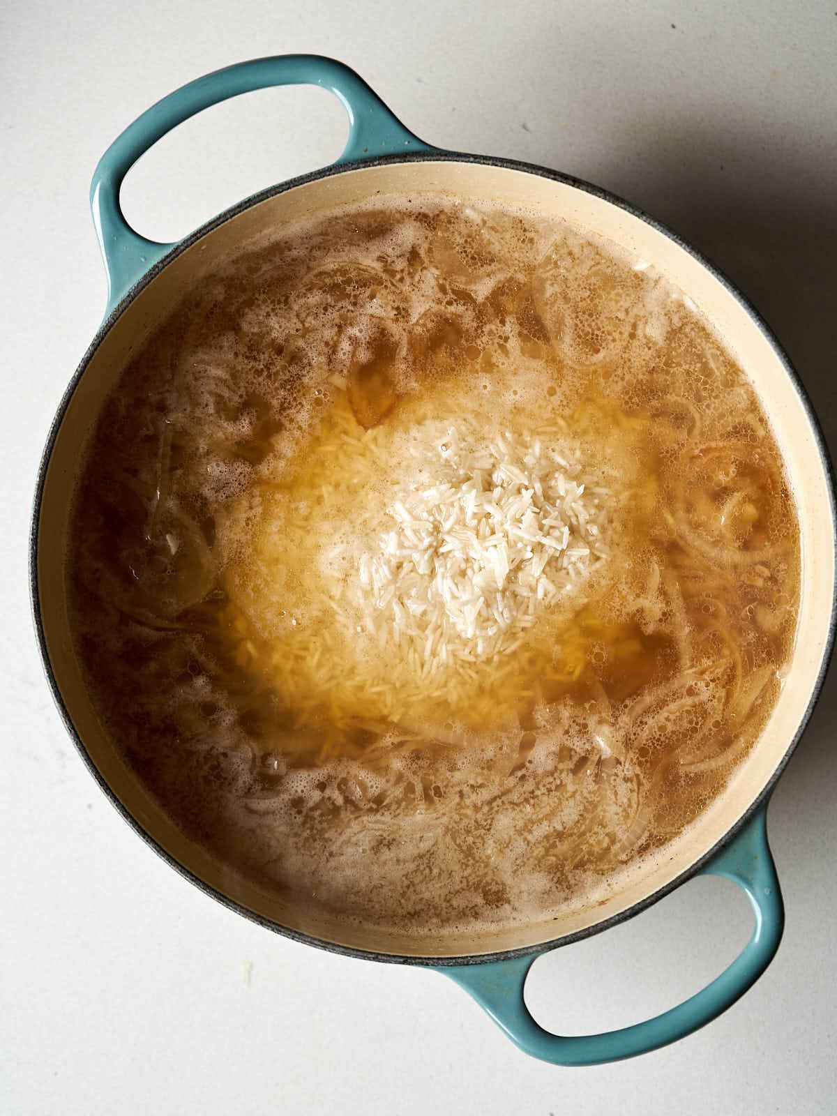 A large dutch oven with warm broth and white rice inside.