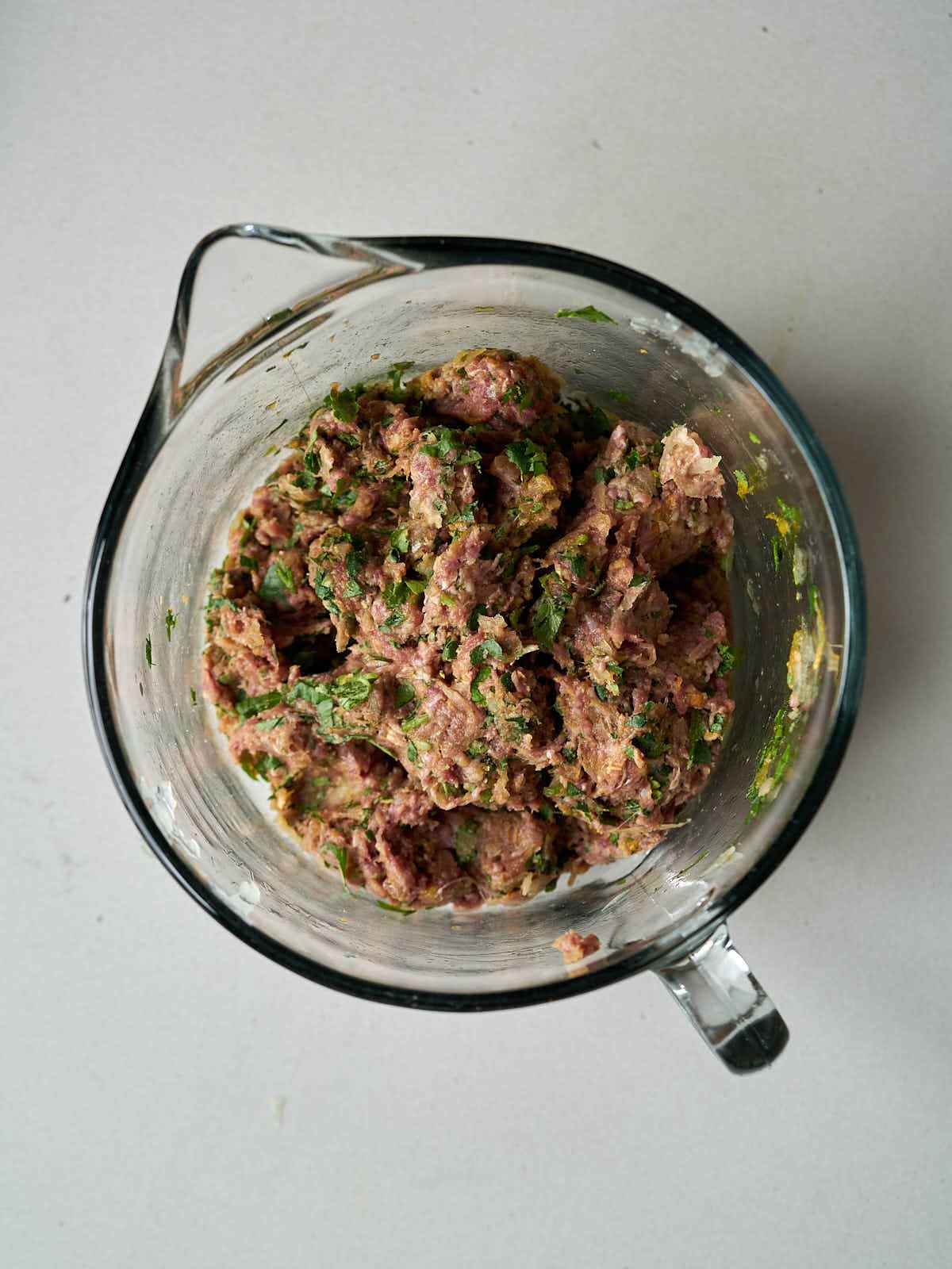 A raw meat and herb mixture in a glass measuring cup.