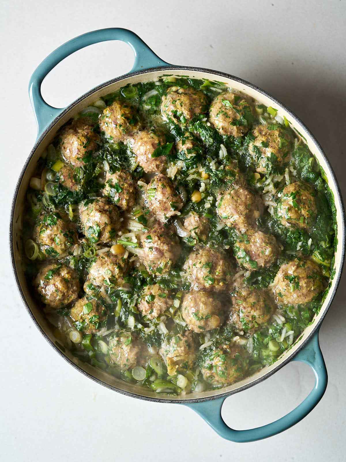 Lots of meat and herb balls in rows inside a dutch oven pot.