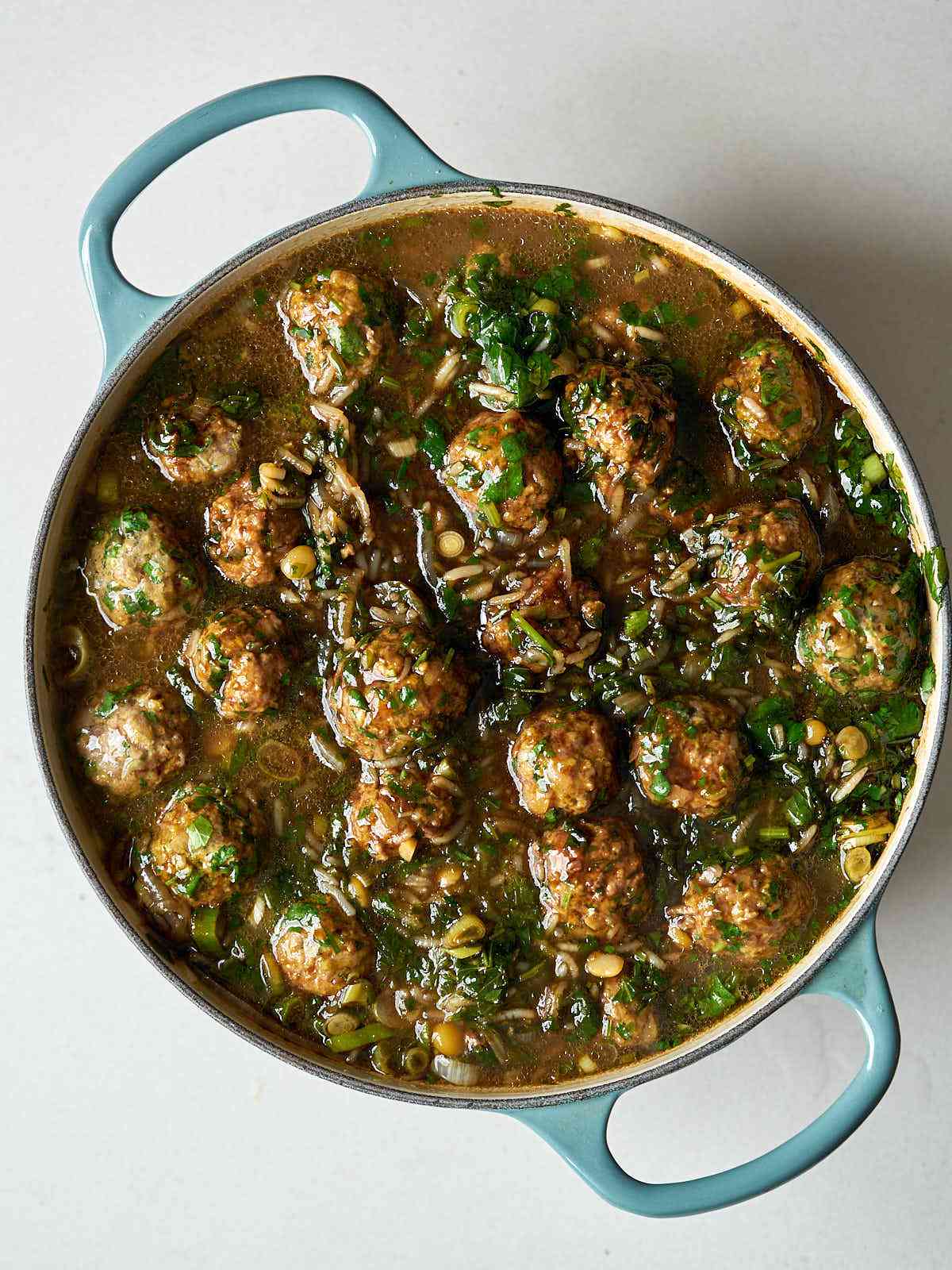 A brown stew with herbs, meatballs, and rice in a large dutch oven.