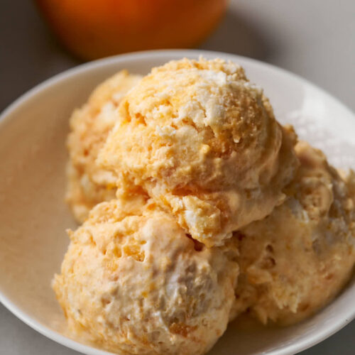 Four scoops of orange semifreddo in a small white bowl next to a persimmon.