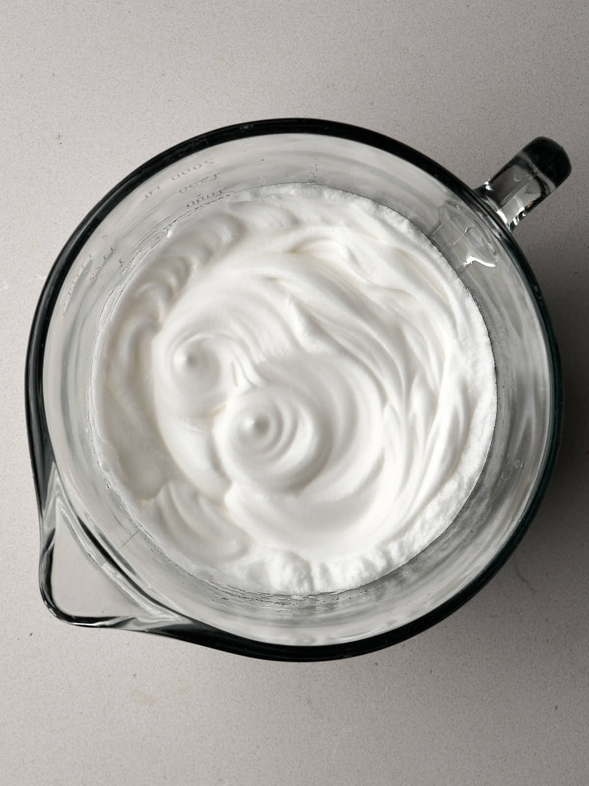 Whipped egg whites in a large glass bowl with a handle and spout.