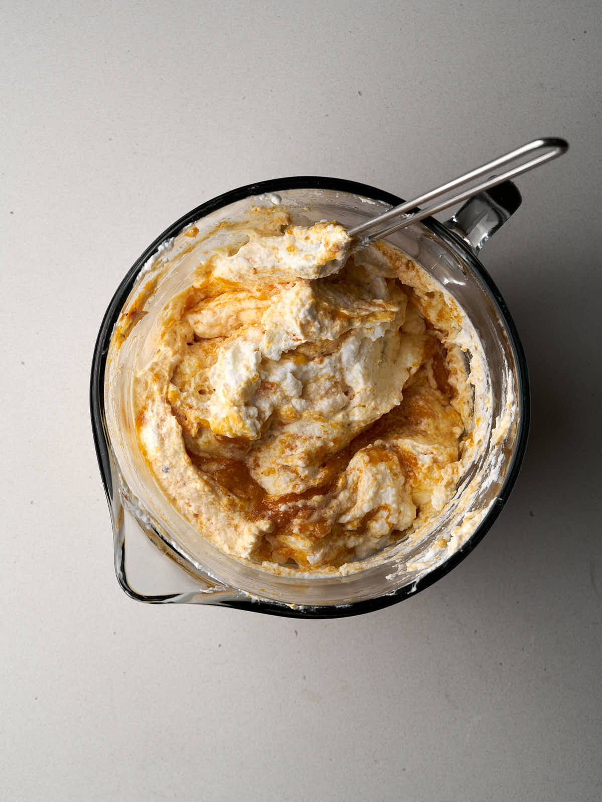 Orange fruit folded into white whipped cream and meringue in a glass bowl with a spout and handle..