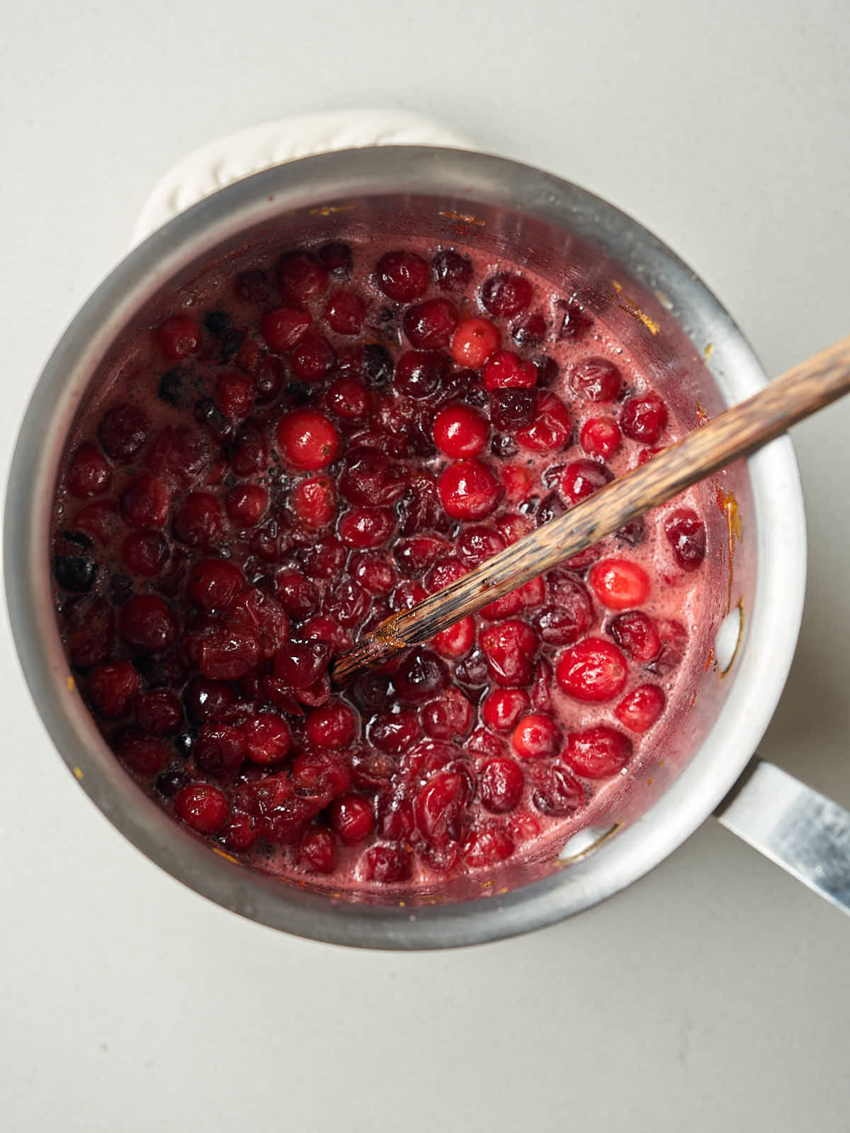 A silver saucepan with red cranberries sizzling, stirred by a wooden spoon.