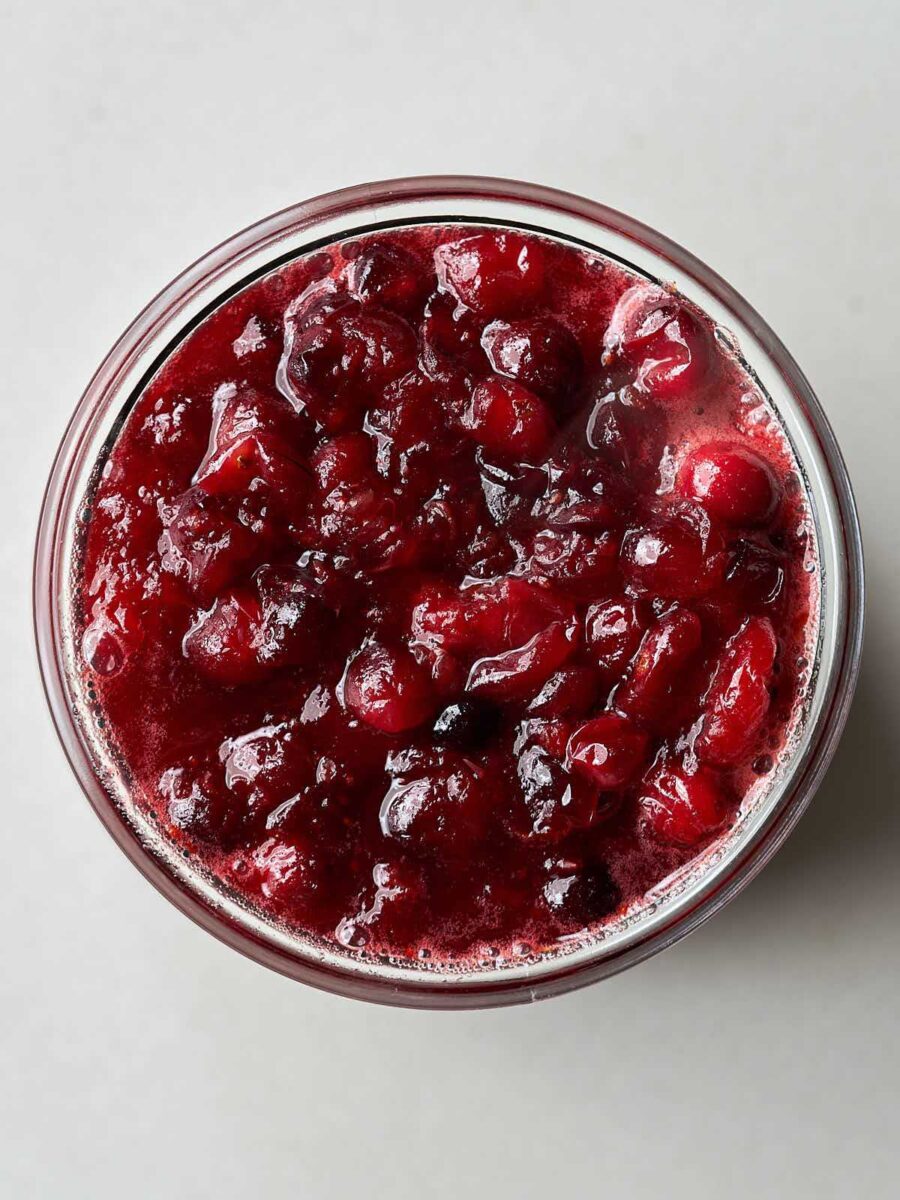 Overhead view of a small glass jar containing chunky red cranberry sauce.